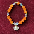 Bracelet with orange beads and a shell charm on a maroon background
