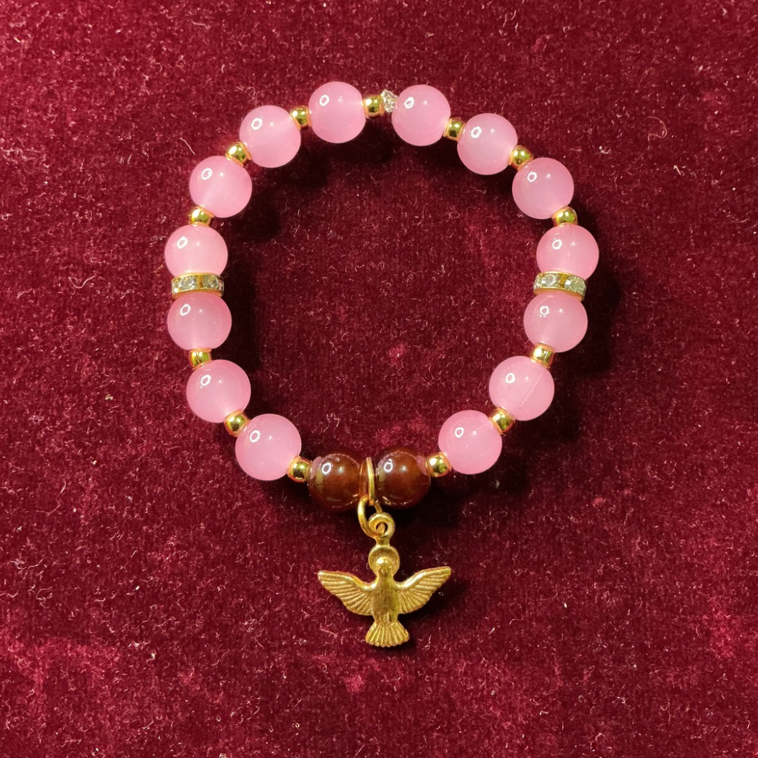 Pink beaded bracelet with a gold dove charm on a red background