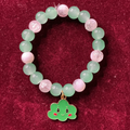 Bracelet with green and pink beads and a smiling clover charm on a red background