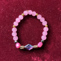 Pink beaded bracelet with a decorative crystal on a maroon background